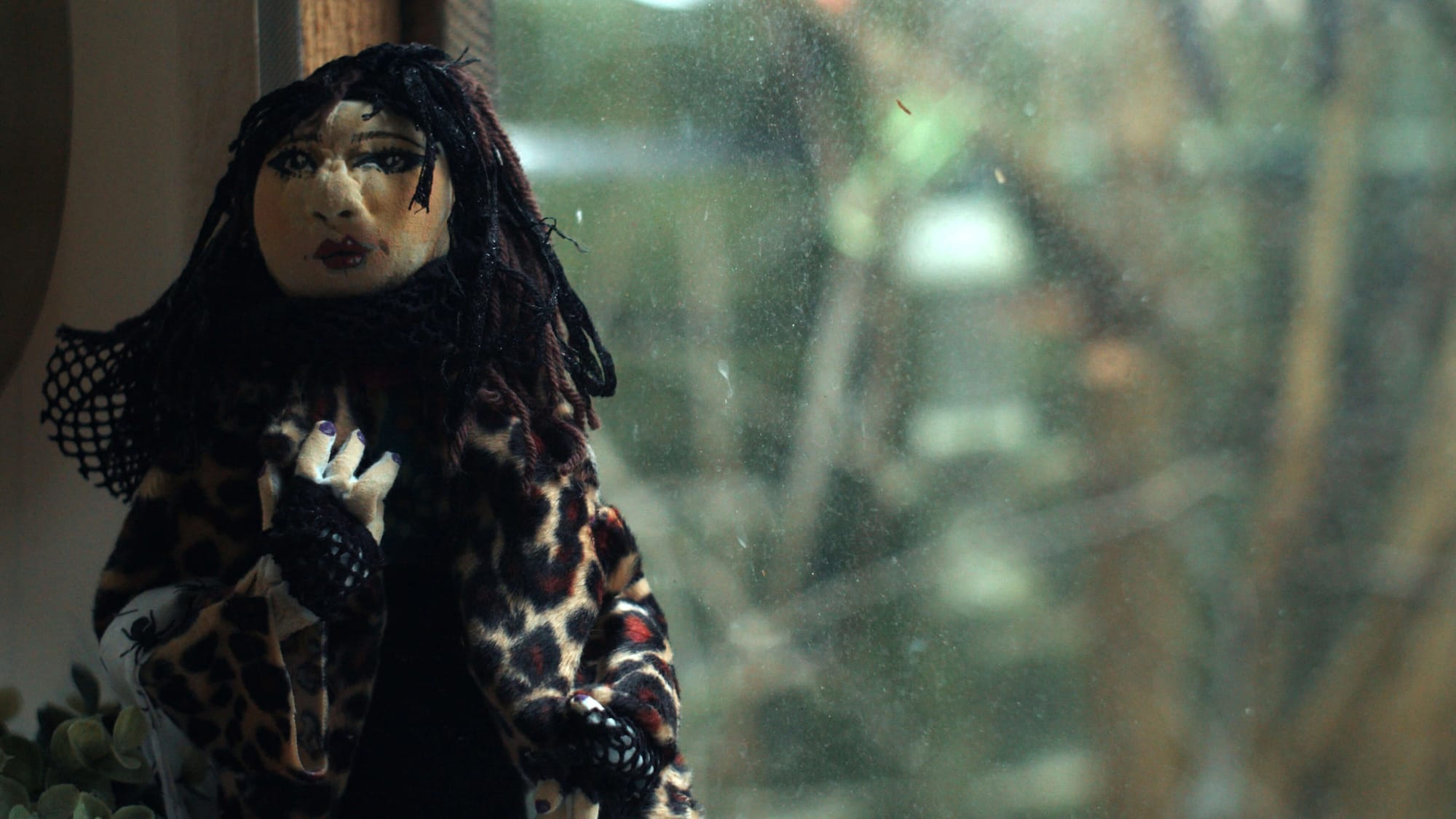 A handmade doll with dark hair and a leopard coat by a window