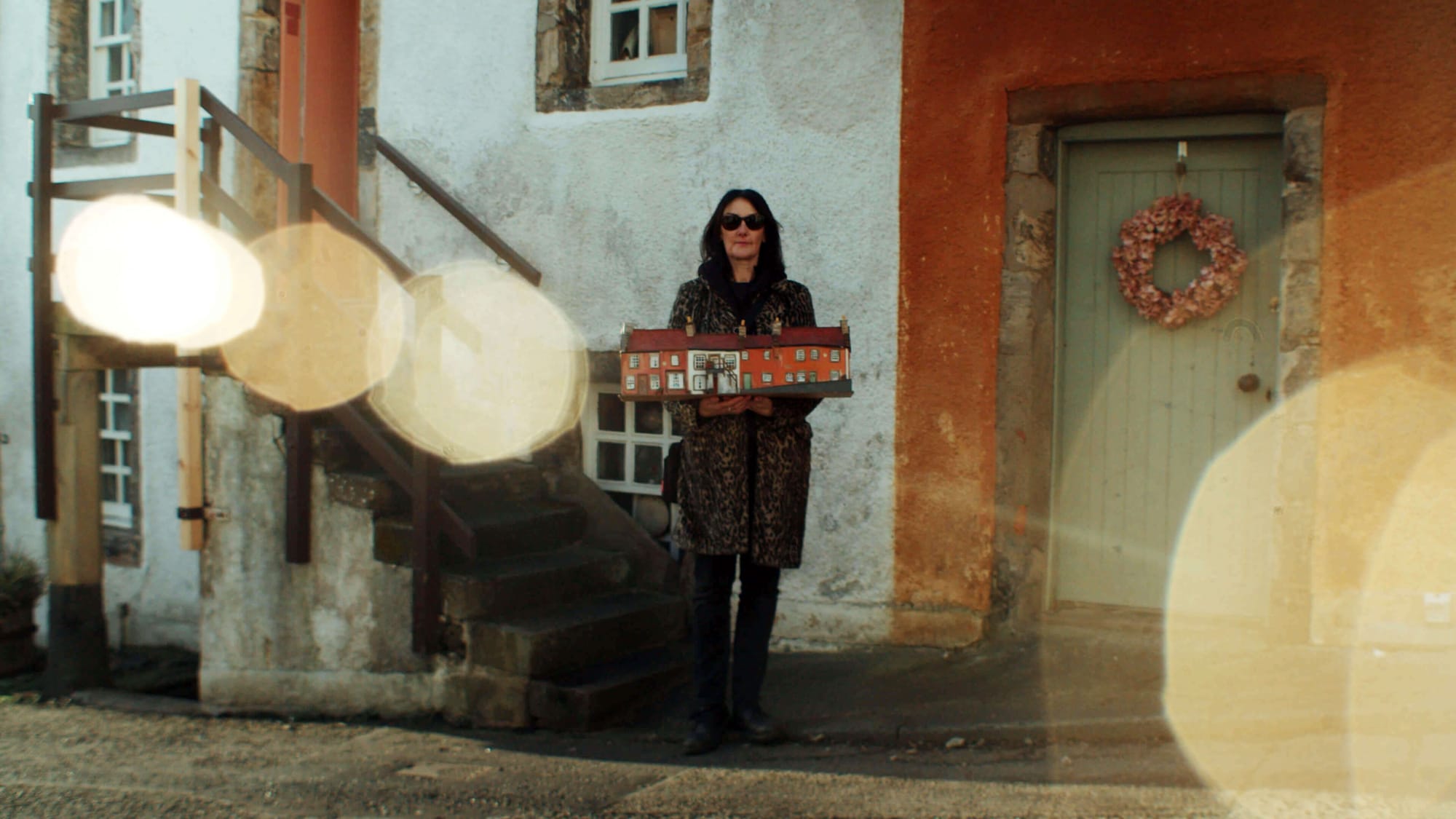 A woman holding a miniature house model outside a rustic building in Culross, Scotland