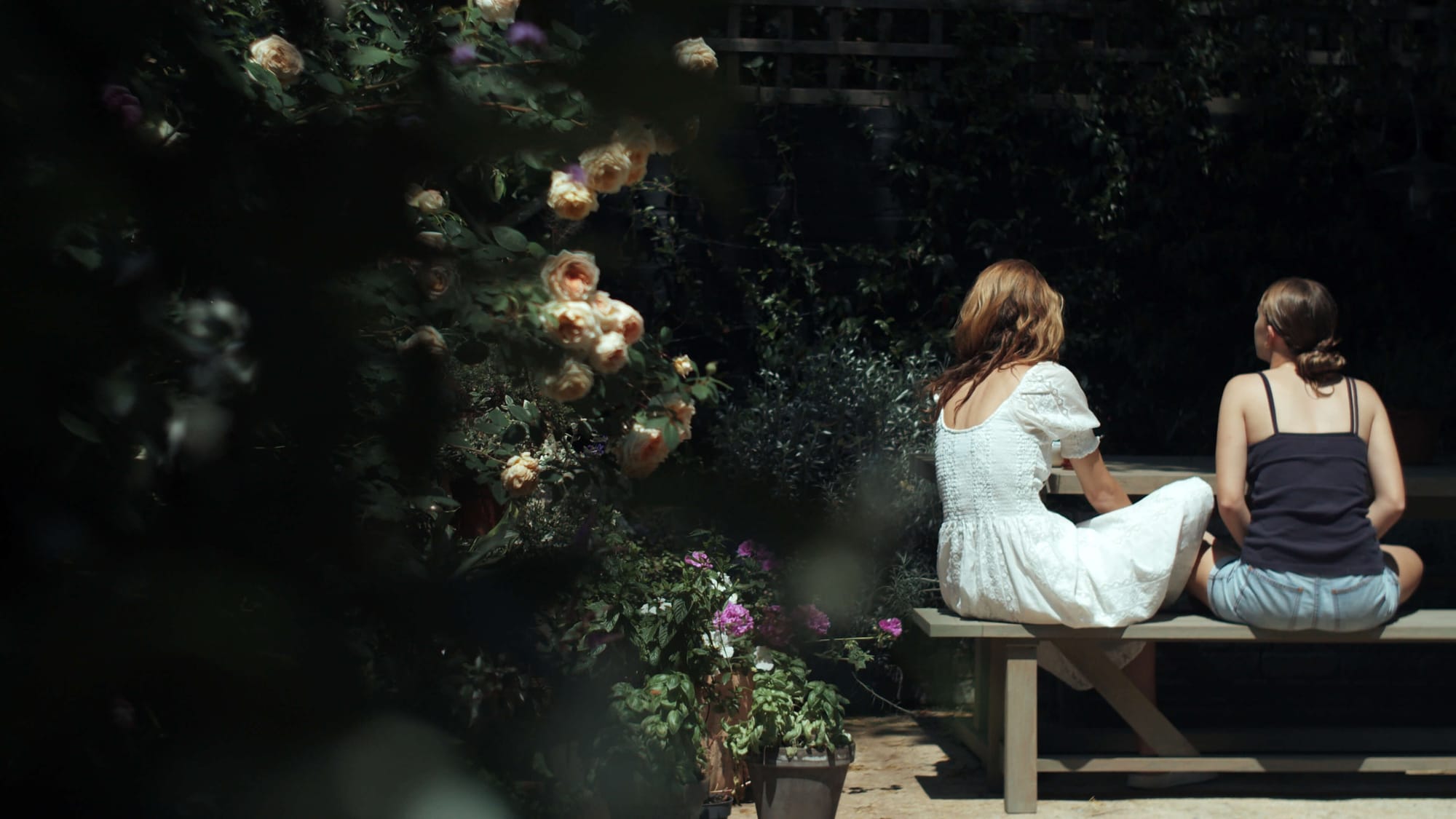 Leanne Kilroy and her daughter sitting on a garden bench surrounded by roses and summer plants