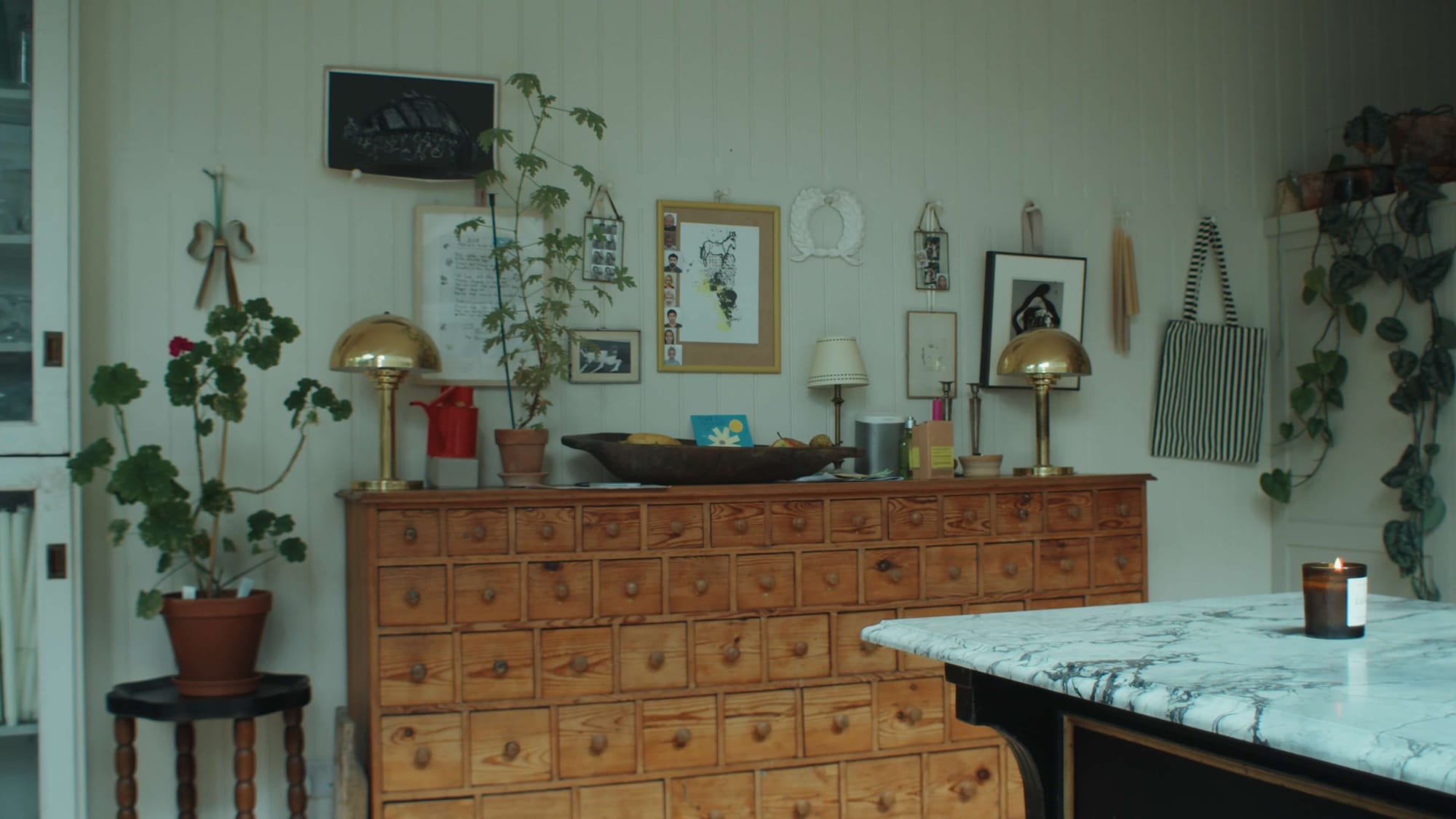 A vintage wooden apothecary chest lined with tiny drawers, topped with plants, brass lamps and family bits and pieces