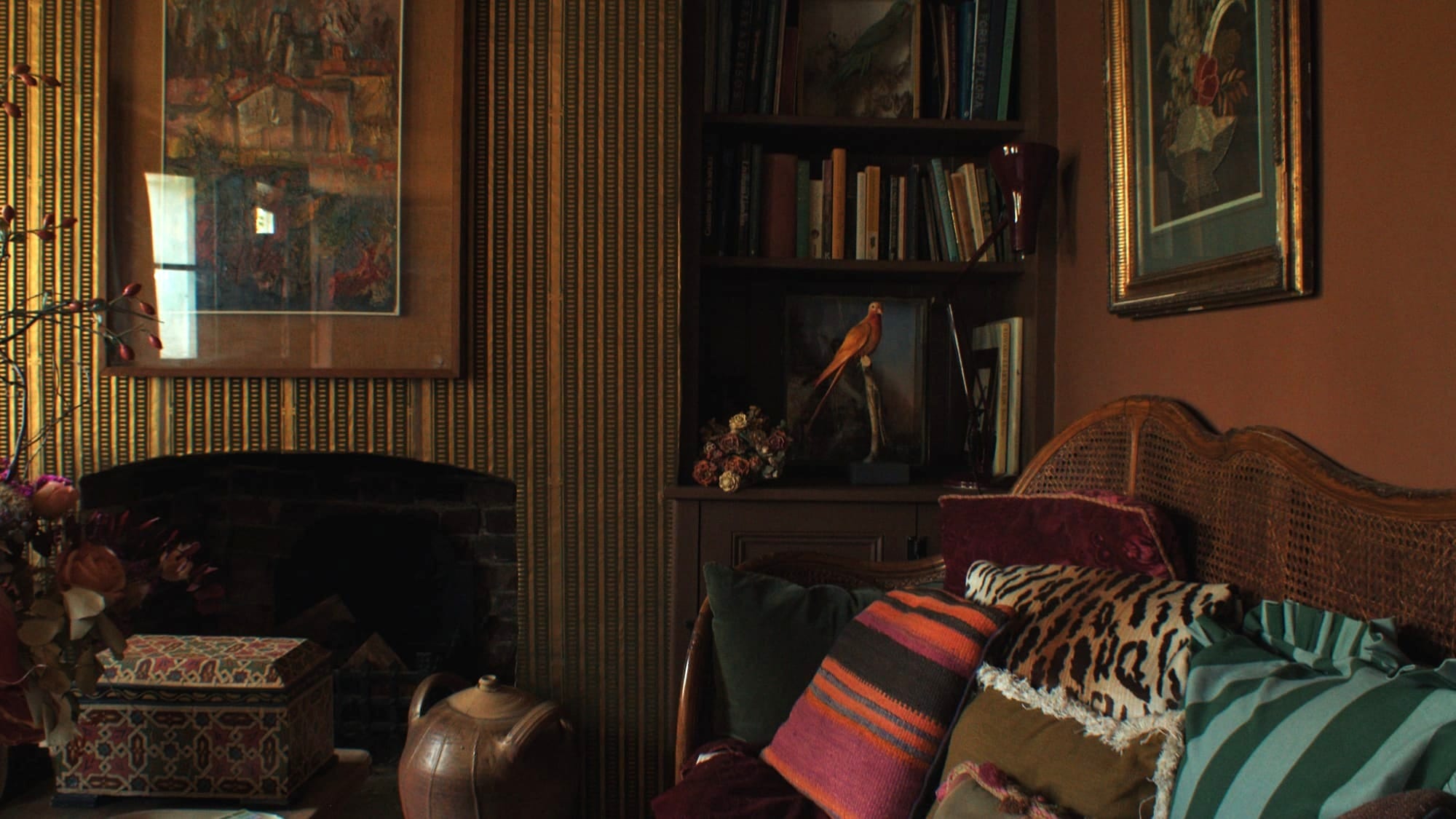 Warm, richly layered living room with patterned cushions, woven sofa, bookshelves, artwork, and vintage objects in earthy Italian-inspired colours