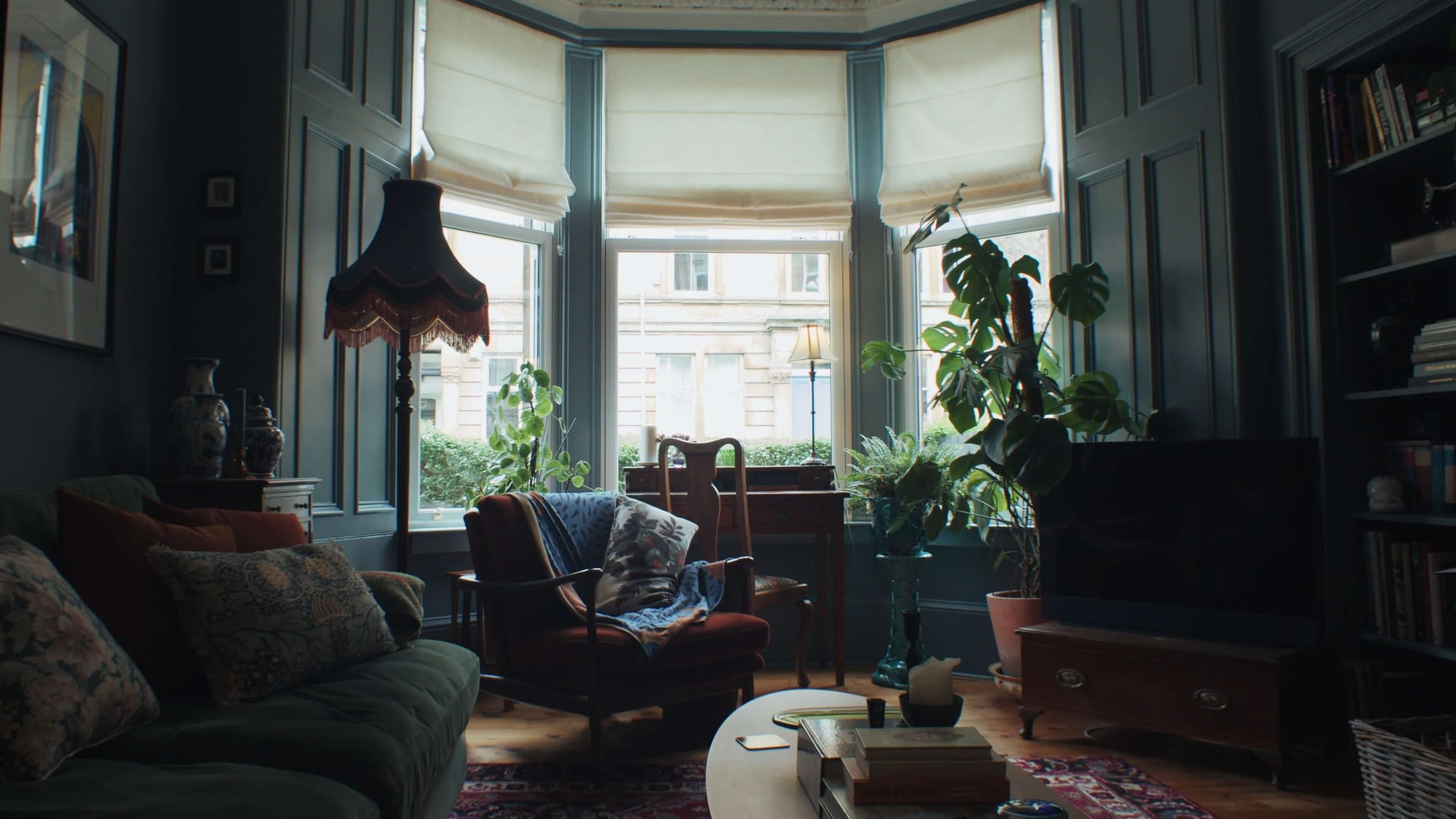 Victorian bay-window living room with dark panelling, vintage furniture, and abundant houseplants creating a calm, layered space