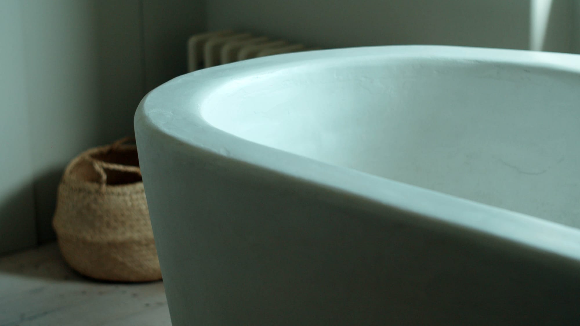 Close-up of a curved freestanding bath with a woven basket beside it
