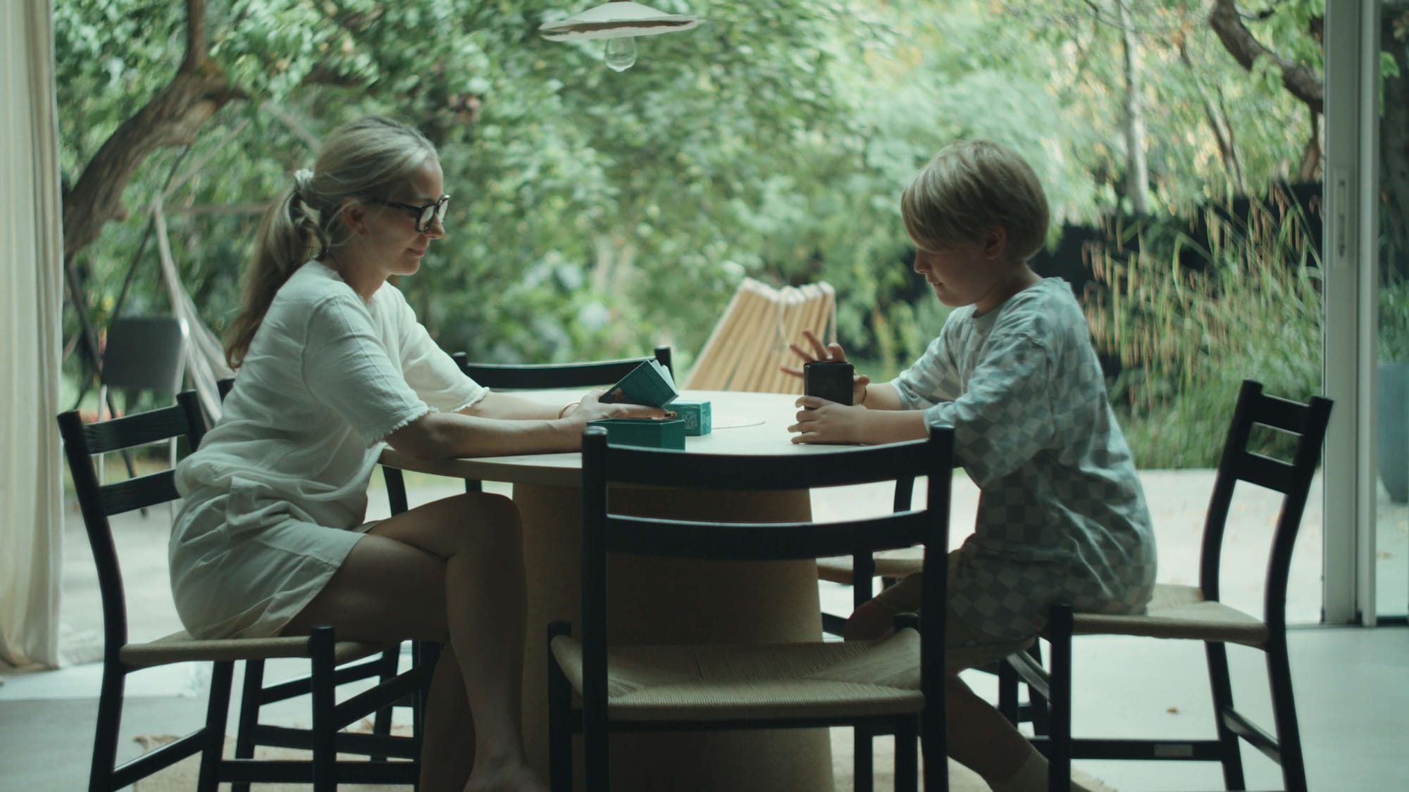 Louisa Grey sitting at a round table with her son Huxley, holding cups in a dining room opening onto a garden
