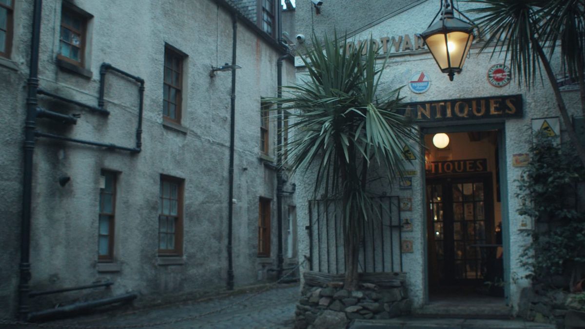 The entrance to Courtyard Antiques, a hidden Edinburgh shop with a vintage sign, warm lighting, and palm trees in a quiet cobbled courtyard