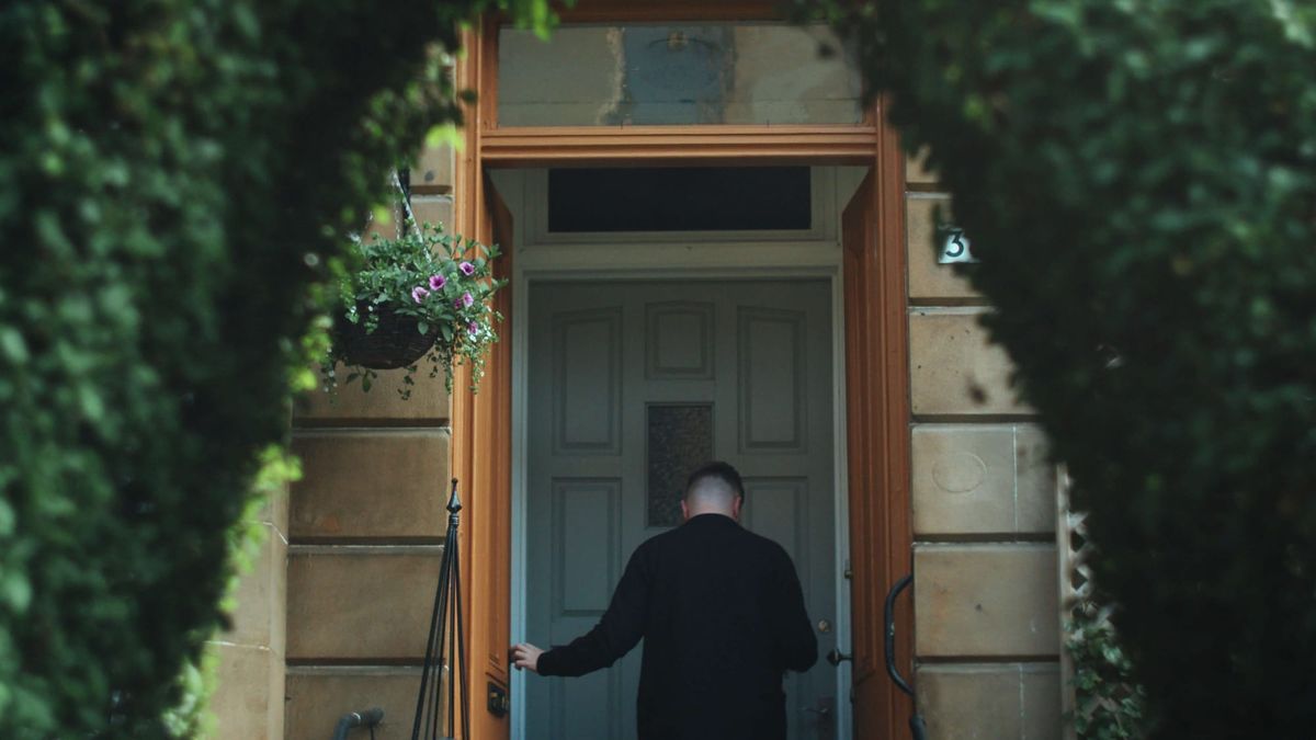 Man entering a Victorian tenement doorway in Glasgow framed by greenery and hanging flowers