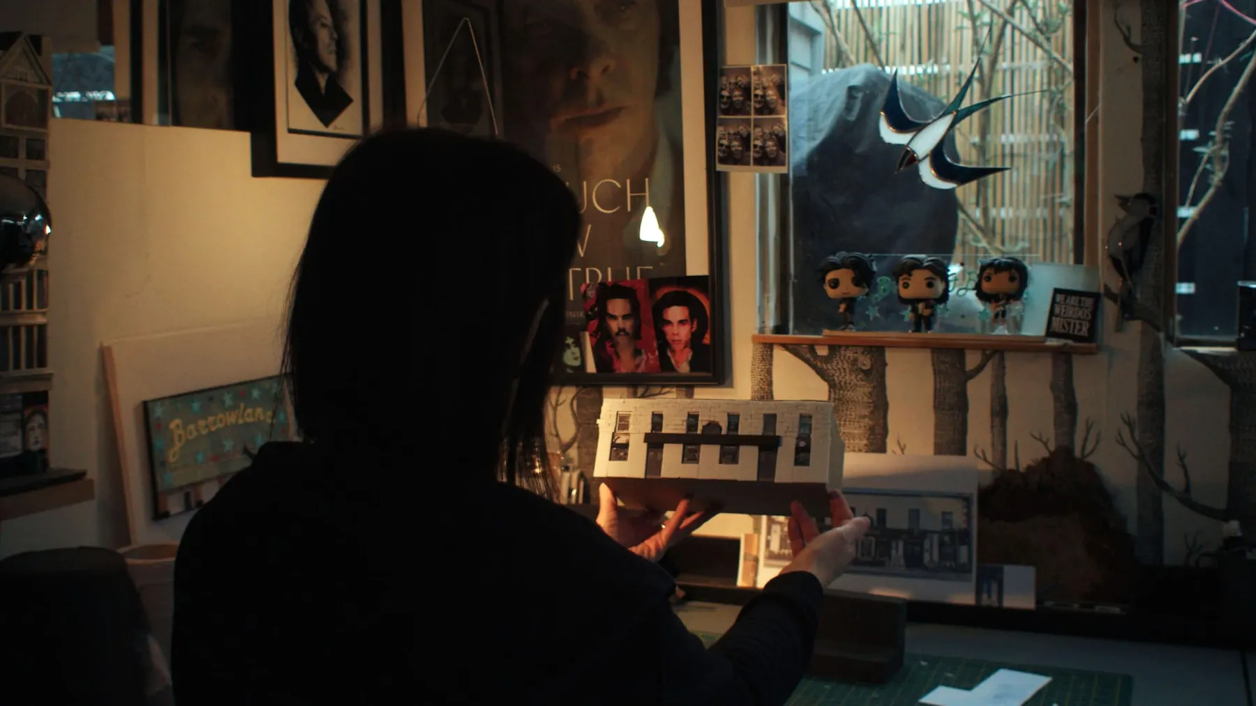 Karen Bones holding a miniature model of a building in a dimly lit room