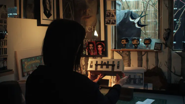 Karen Bones holding a miniature model of a building in a dimly lit room