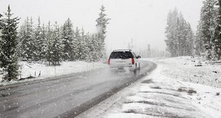 A vehicle drives along a snow-covered road during snowfall