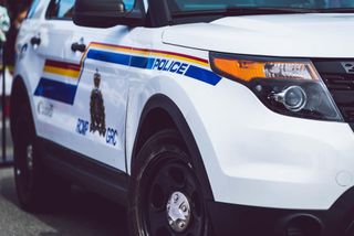 Close-up of a white RCMP police SUV showing the force's crest, RCMP GRC lettering, and red, yellow and blue stripes along the door.