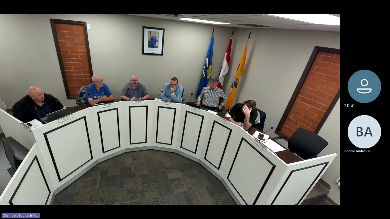 Six people seated at a curved council dais in Redcliff's council chambers during a regular council meeting, with flags visible behind them.