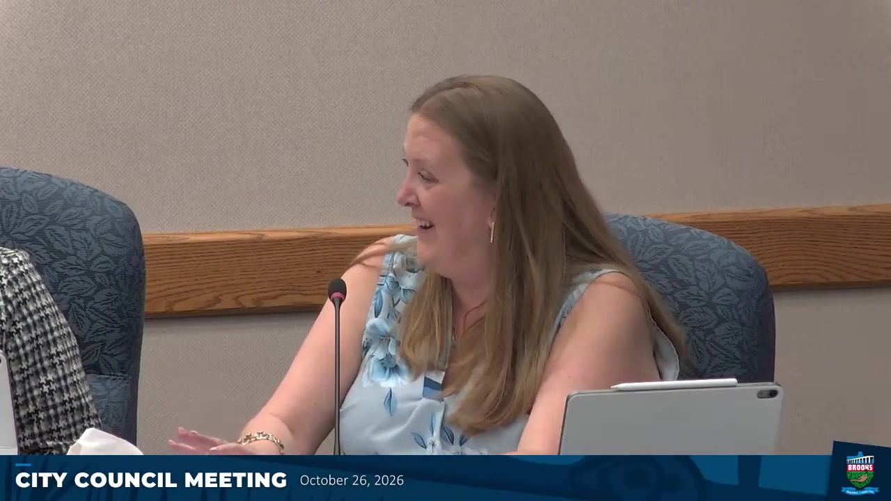 A woman with long brown hair speaks into a microphone at a Brooks city council meeting on Oct. 26, 2026, identified as Coun. Johnson.