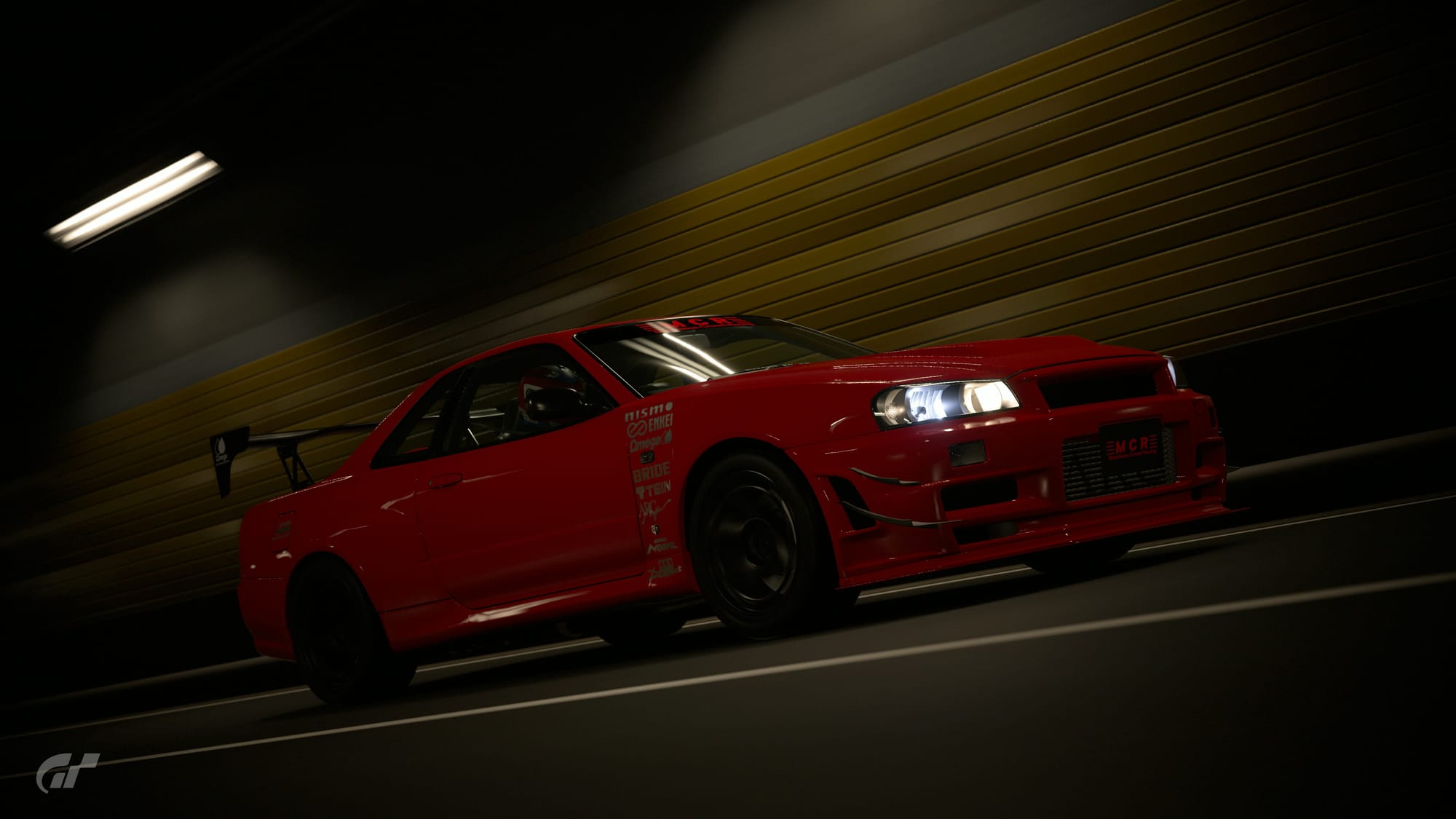 A red Nissan Skyline GT-R R34 NISMO Z-Tune driving in a tunnel. The car has been modified to resemble the MCR R34 with a GT-style rear wing and front bumper, and has silver decals on the rear of the front fenders.