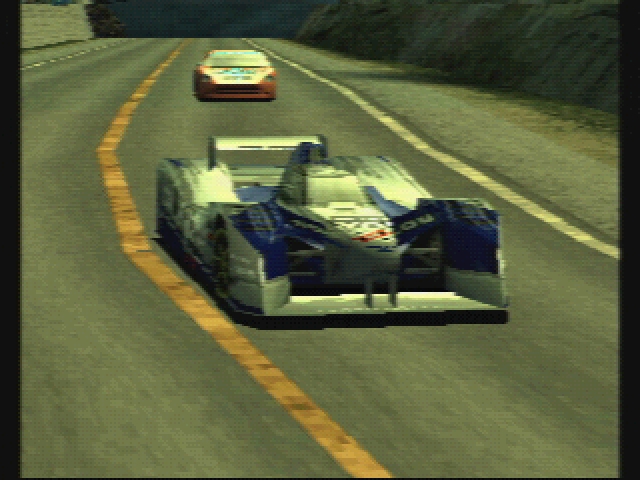 A sceenshot from Ridge Racer Type 4. In it we have a silver and blue Assoluto Squalo prototype race car being chased by a orange Âge Megere sports car along a mountain road.