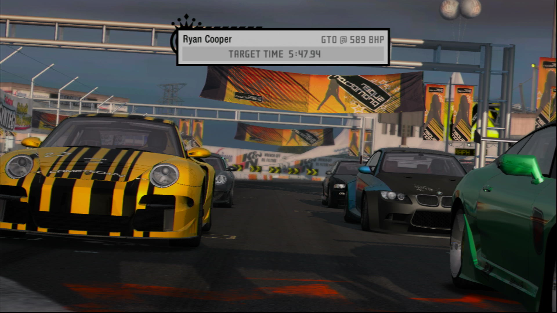 The pre-grid cinematic for a grip race in Need For Speed Pro Street, with the camera walking backwards showing all the cars as they're on the grid. On the penultimate row, that's currently visible, is a yellow Porsche 911 and a black and blue BMW M3.