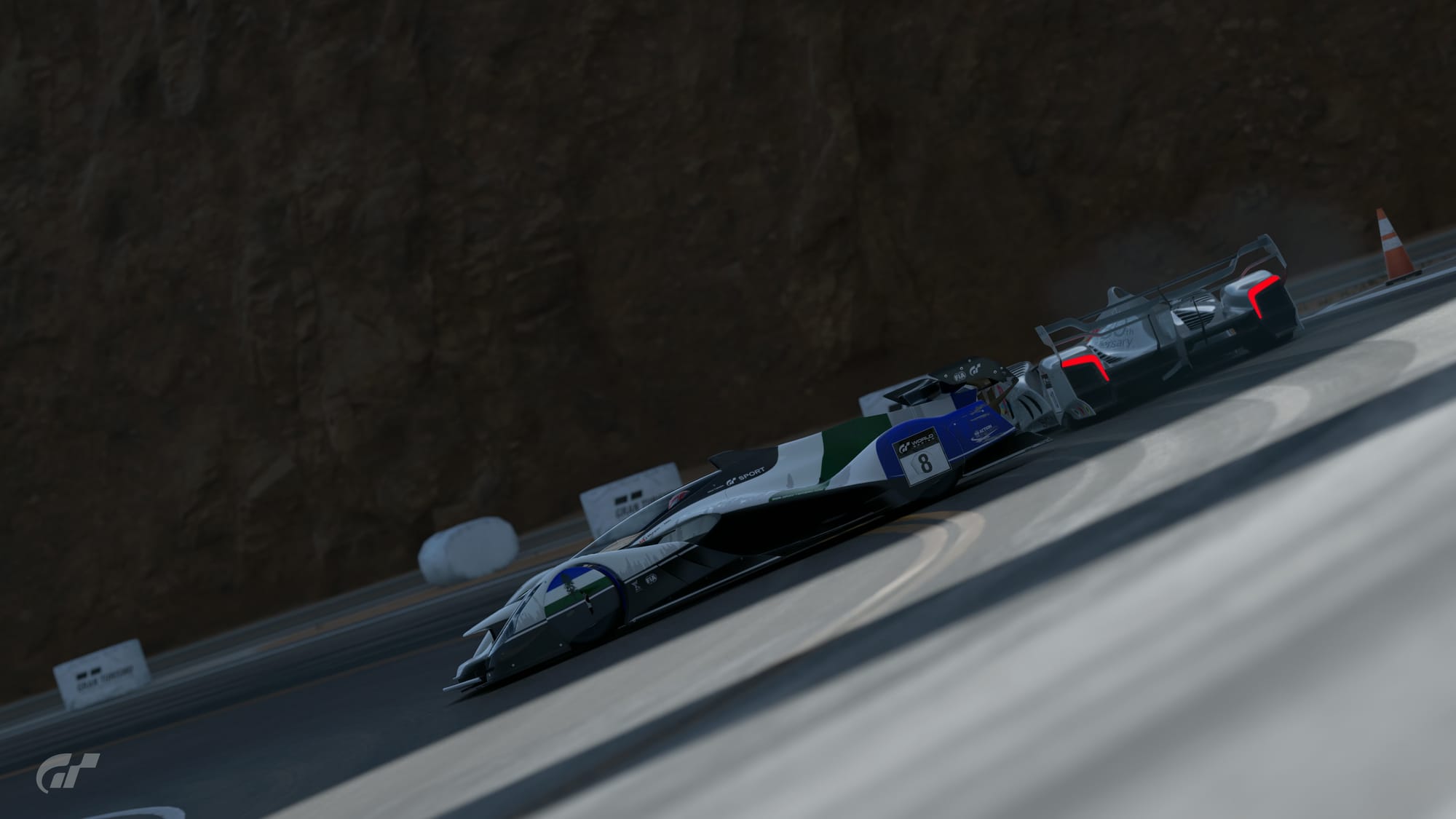 The white, with blue and green Red Bull X2019 formula-style racing car spinning by itself, with a car on it's outside, at the last turn of Grand Valley Highway 1 reverse.