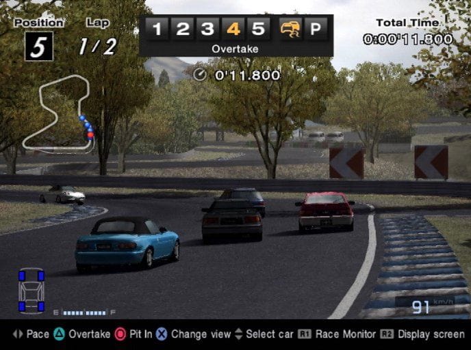 Five cars navigate the first turn of Autumn Ring Mini Reverse in a B-Spec race in Gran Turismo 4, the player-dictated pace is set to it's second highest level and the ai driver is being told to overtake.