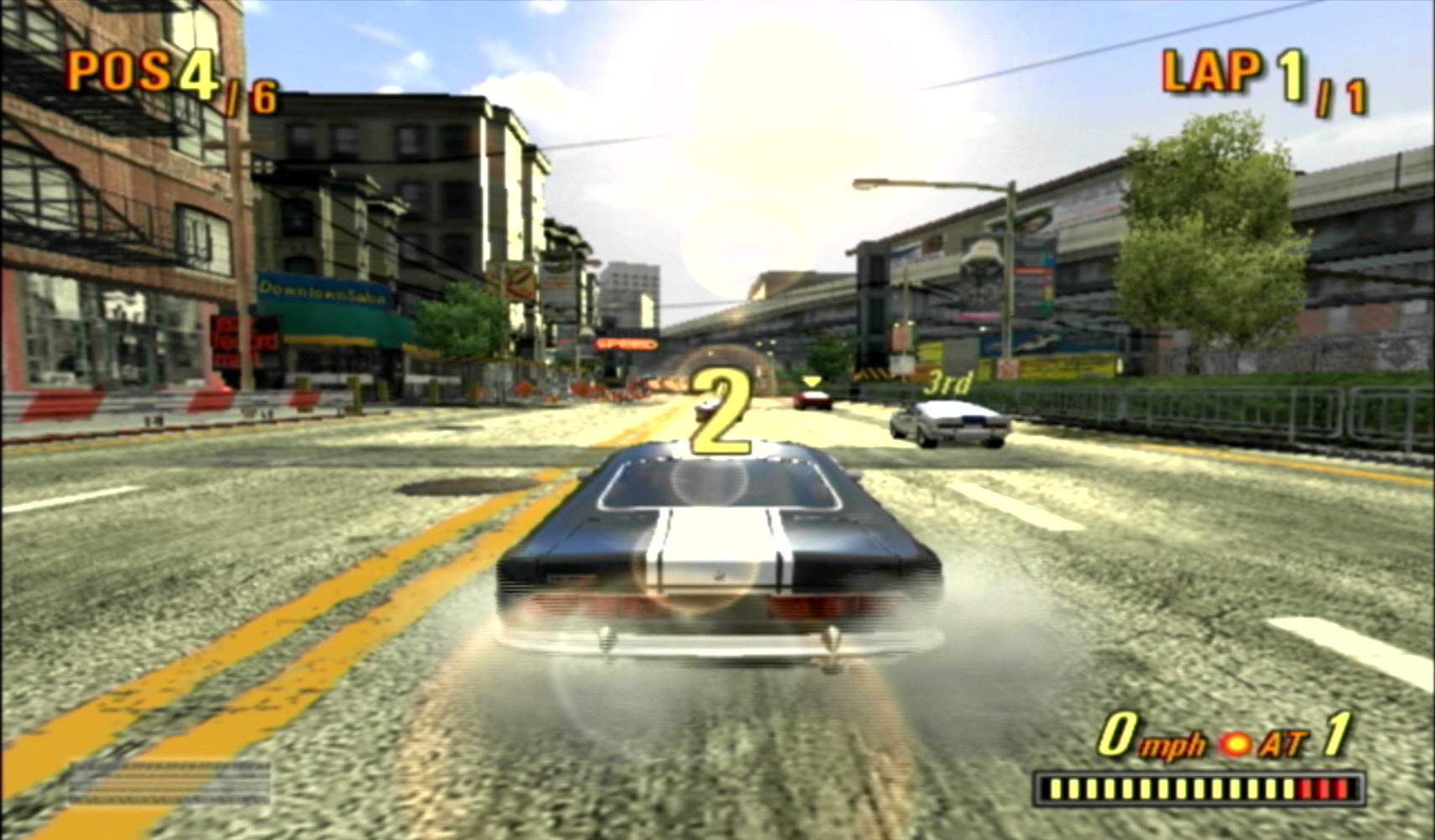 The start of a race in the Burnout 3 demo. The black muscle car the player is driving is doing a standing burnout with the rev bar maxed out on the bottom right. It still shows the car in first gear and using the automatic transmission option.