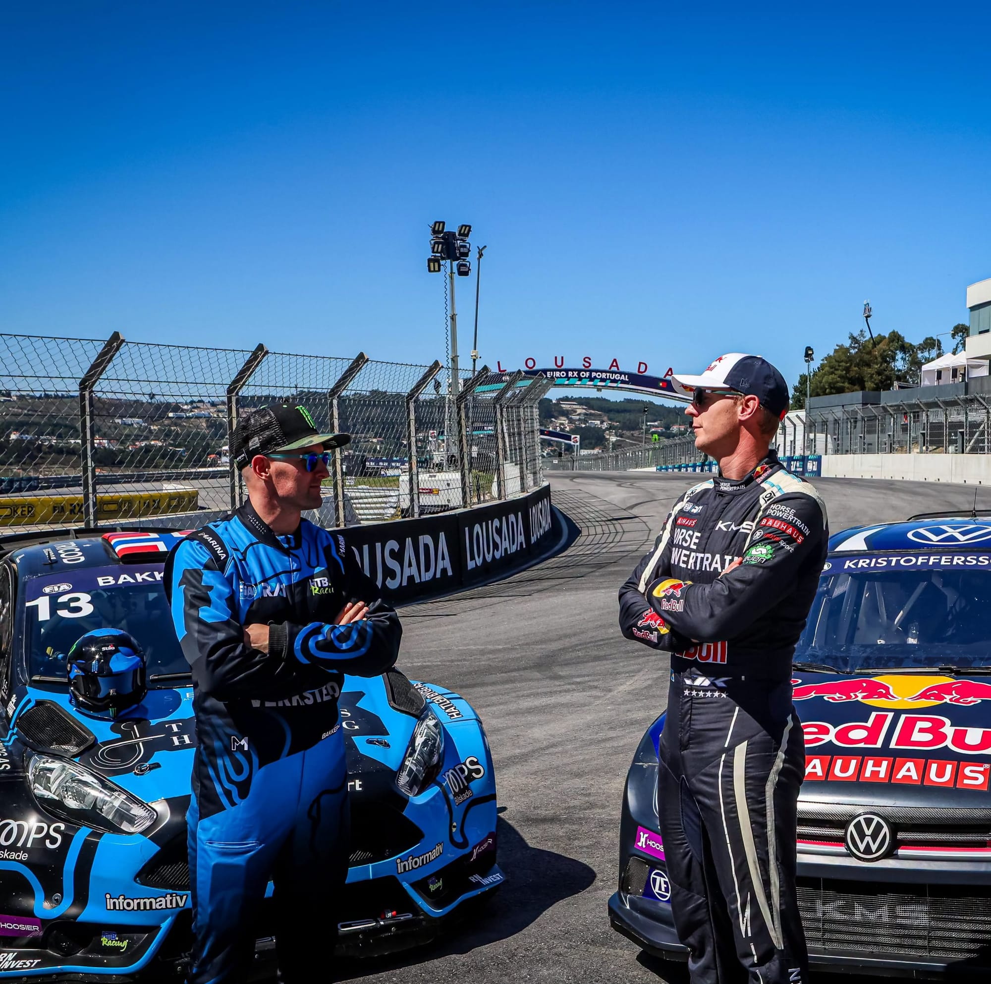 A staged photo with Andreas Bakkerud and Johan Kristoffersson staring at each other, with their respective rallycross supercars behind them.