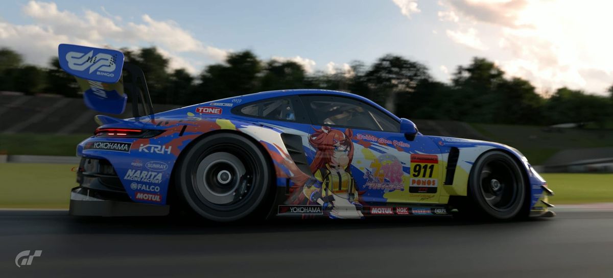 A side shot of the Bubble Gum Fellow Umamusume Porsche 911 GT3 R while it's driving at Suzuka. The car is blue with white, yellow and orange.