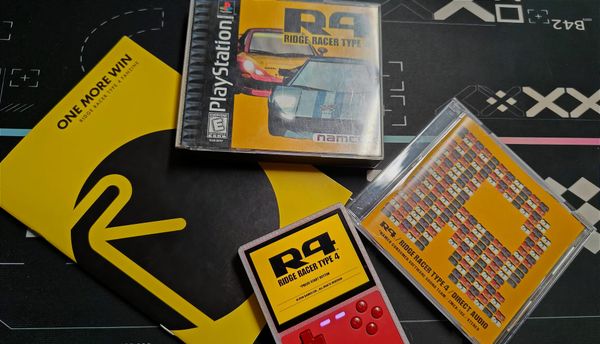 A collection of Ridge Racer Type 4 items on a table. There is a copy of the game, the Direct Audio CD, One More Win fanzine and R4 playing on a Trimui Brick.