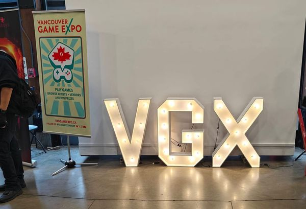 The VGX light up sign against a pull down projector wall, with the Vancouver Game Expo event banner alongside.