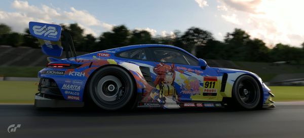 A side shot of the Bubble Gum Fellow Umamusume Porsche 911 GT3 R while it's driving at Suzuka. The car is blue with white, yellow and orange.