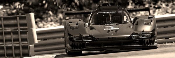 A Porsche 963 Le Mans Prototype race car entering the chicane at Watkens Glen International, with the armco barrier at the start of that corner sequence to it's inside.
