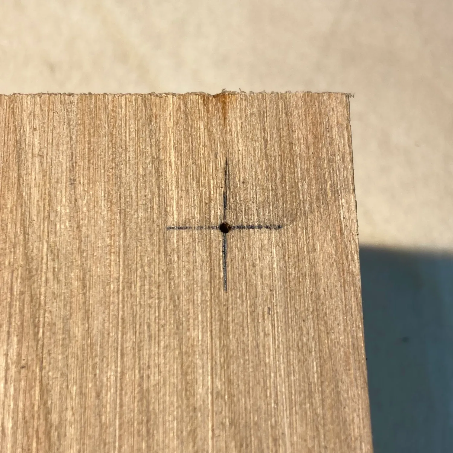 An image showing the center point for a hole marked with a cross drawn with a pencil and indented with an awl.