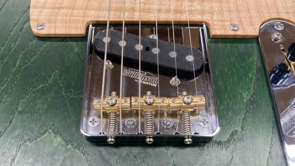 A close-up image of a Wilkinson by Gotoh bridge mounted on a green guitar.