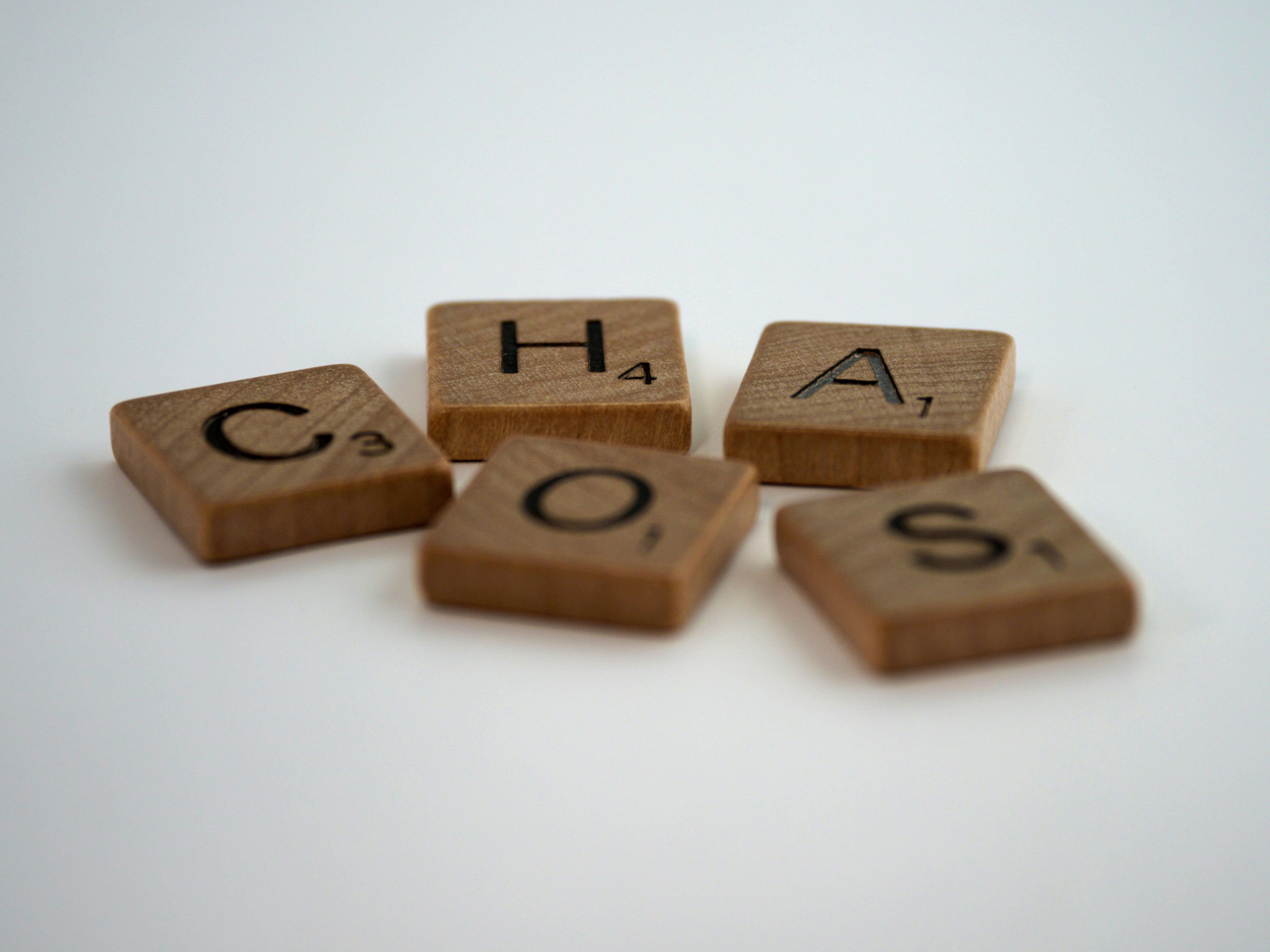 Scrabble tiles scattered a bit haphazardly on a white background. They spell out "chaos"