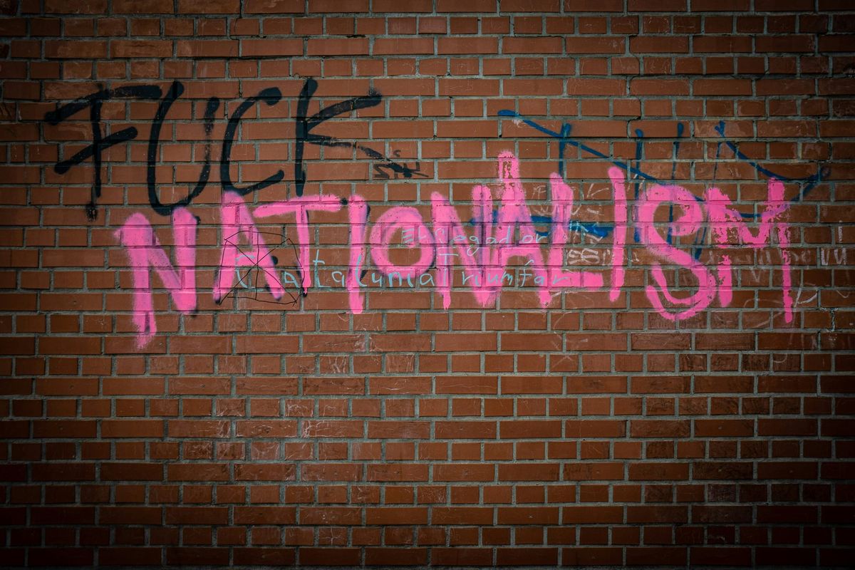 Grafitti that says "FUCK NATIONALISM" in big black ("fuck") and pink ("nationalism") block letters on a red brick wall.