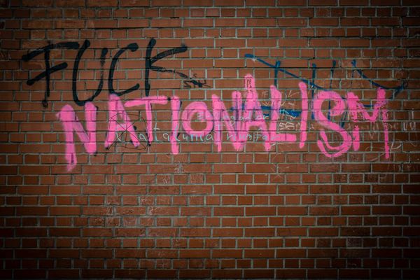 Grafitti that says "FUCK NATIONALISM" in big black ("fuck") and pink ("nationalism") block letters on a red brick wall.
