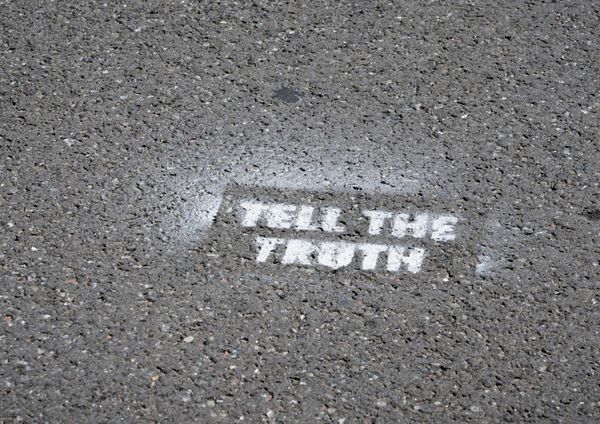 A picture of a section of asphalt with stenciled graffiti on it that reads, in white block letters, "TELL THE TRUTH."