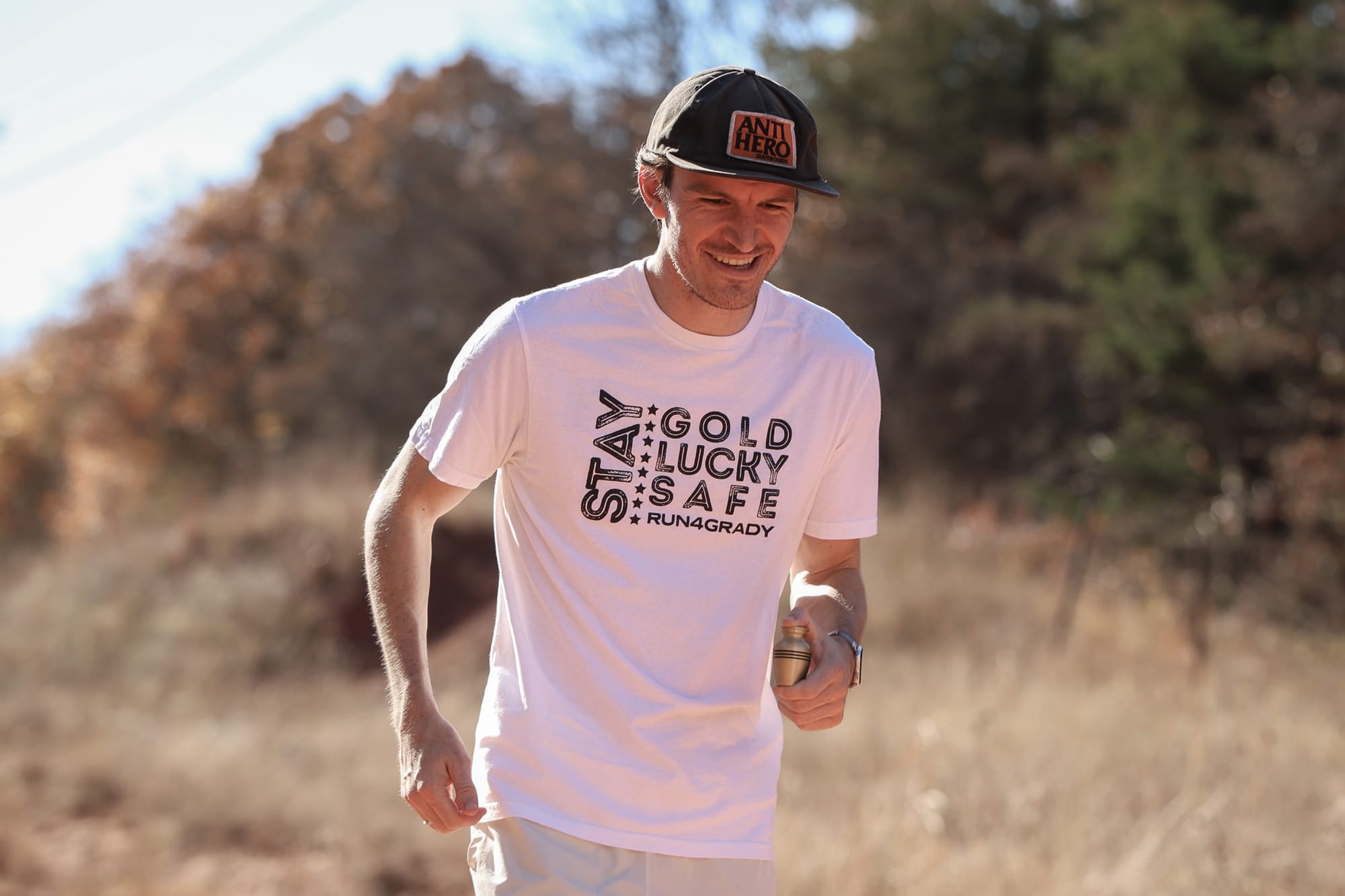 Stone Lambert running, holding brother's urn, wearing t shirt with the words "Stay Gold, Lucky, Safe, Run4Grady