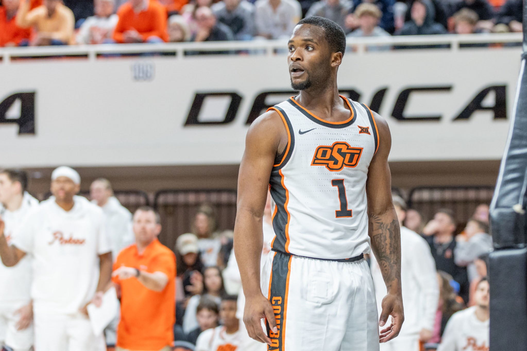  Oklahoma State point guard Kanye Clary (1) in a white OSU jersey looks on during game action at Gallagher-Iba Arena with crowd visible in the background.
