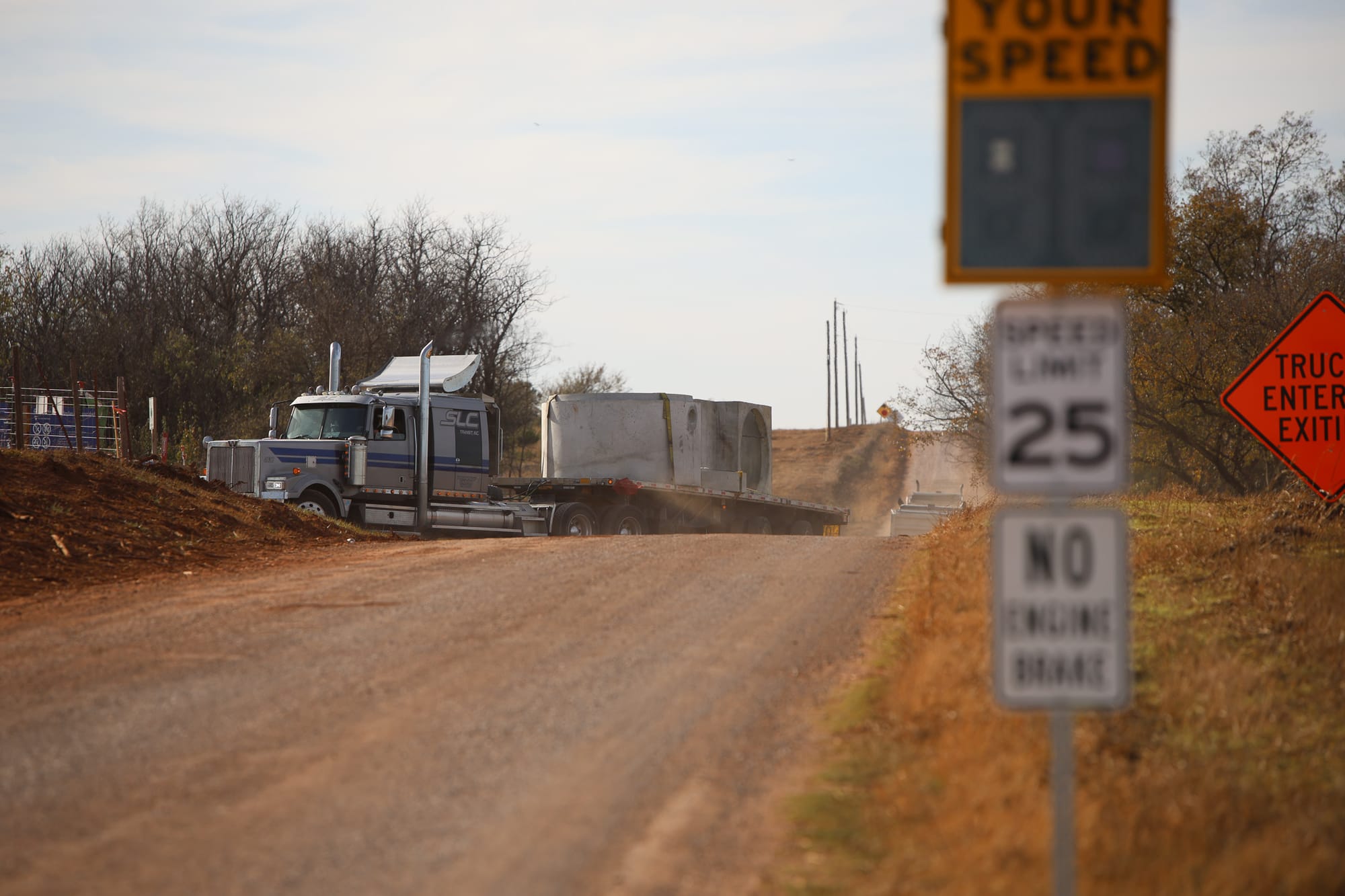 Semi truck carrying concrete components on unpaved Richmond Road, with speed monitoring sign, 25 mph limit, and "No Engine Brake" sign visible along the rural route to Google's data center site.