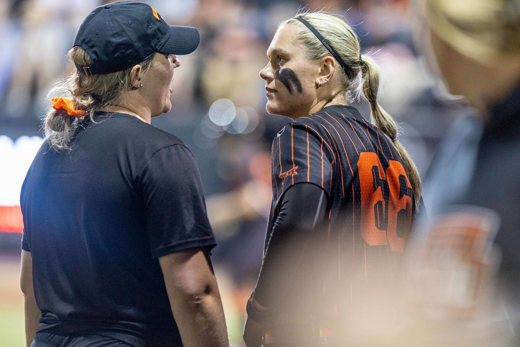 Oklahoma State assistant coach Carrie Eberle Parker in dark cap and shirt talks with pitcher Ruby Meylan in black pinstriped uniform during game at Cowgirl Softball Complex April 23, 2025.