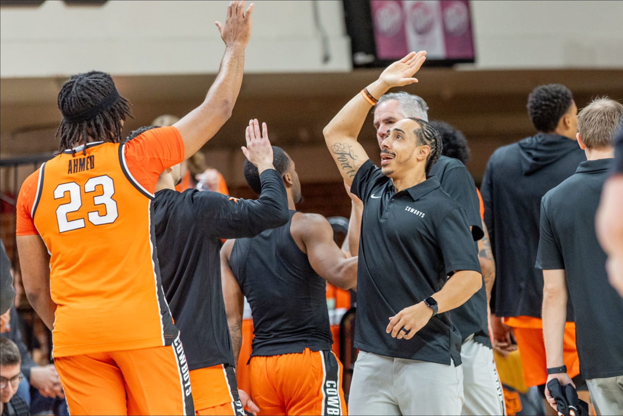 Oklahoma State freshman center Ben Ahmed (23) in orange jersey high-fives strength and conditioning coach Marcus Edwards during a game at Gallagher-Iba Arena.