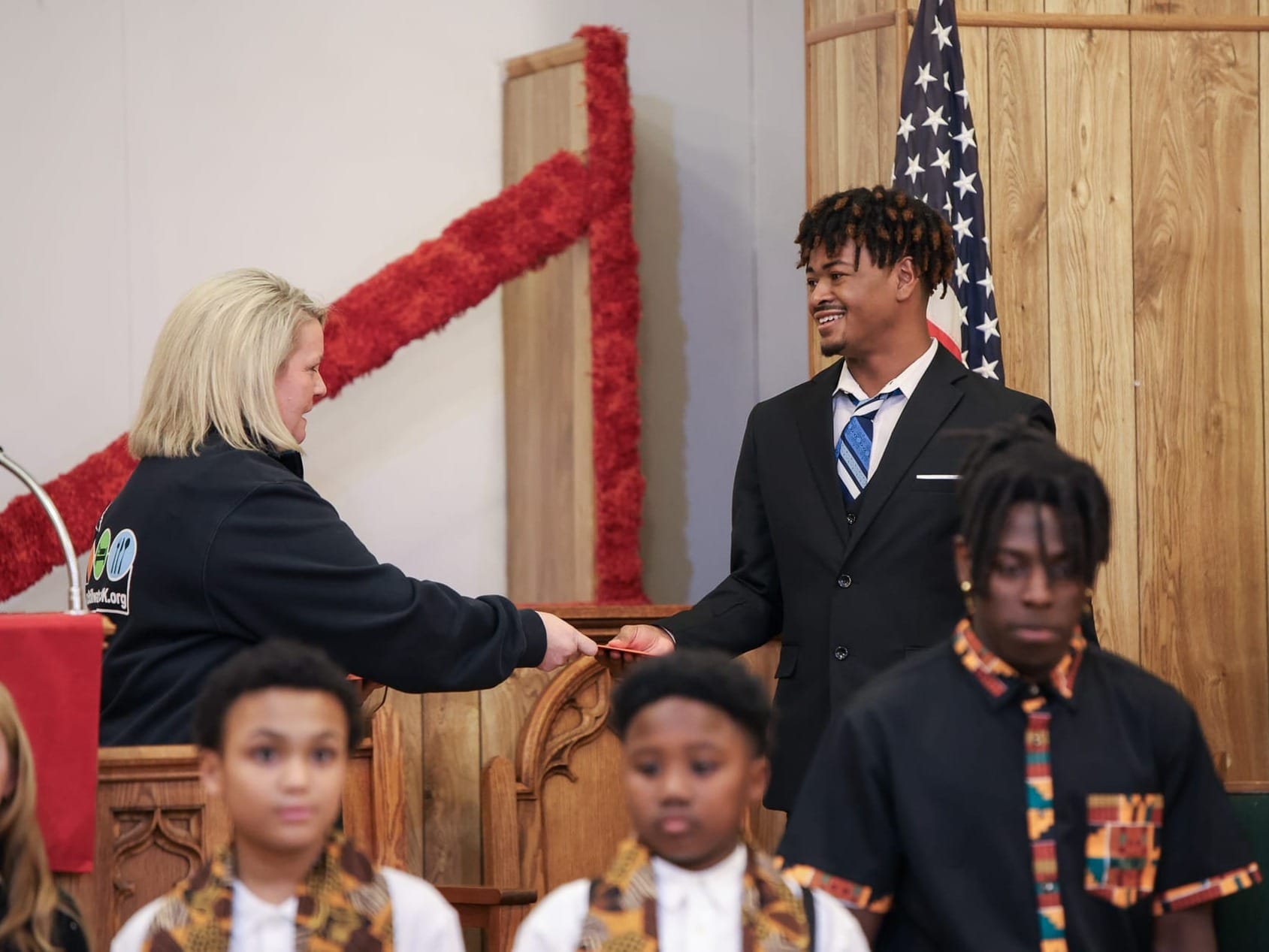 Cristy Morrison presents gift card to Jamiere Dickens-Smith following his speech at Mt. Zion Baptist Church during MLK Jr. Day celebration with youth speakers in foreground