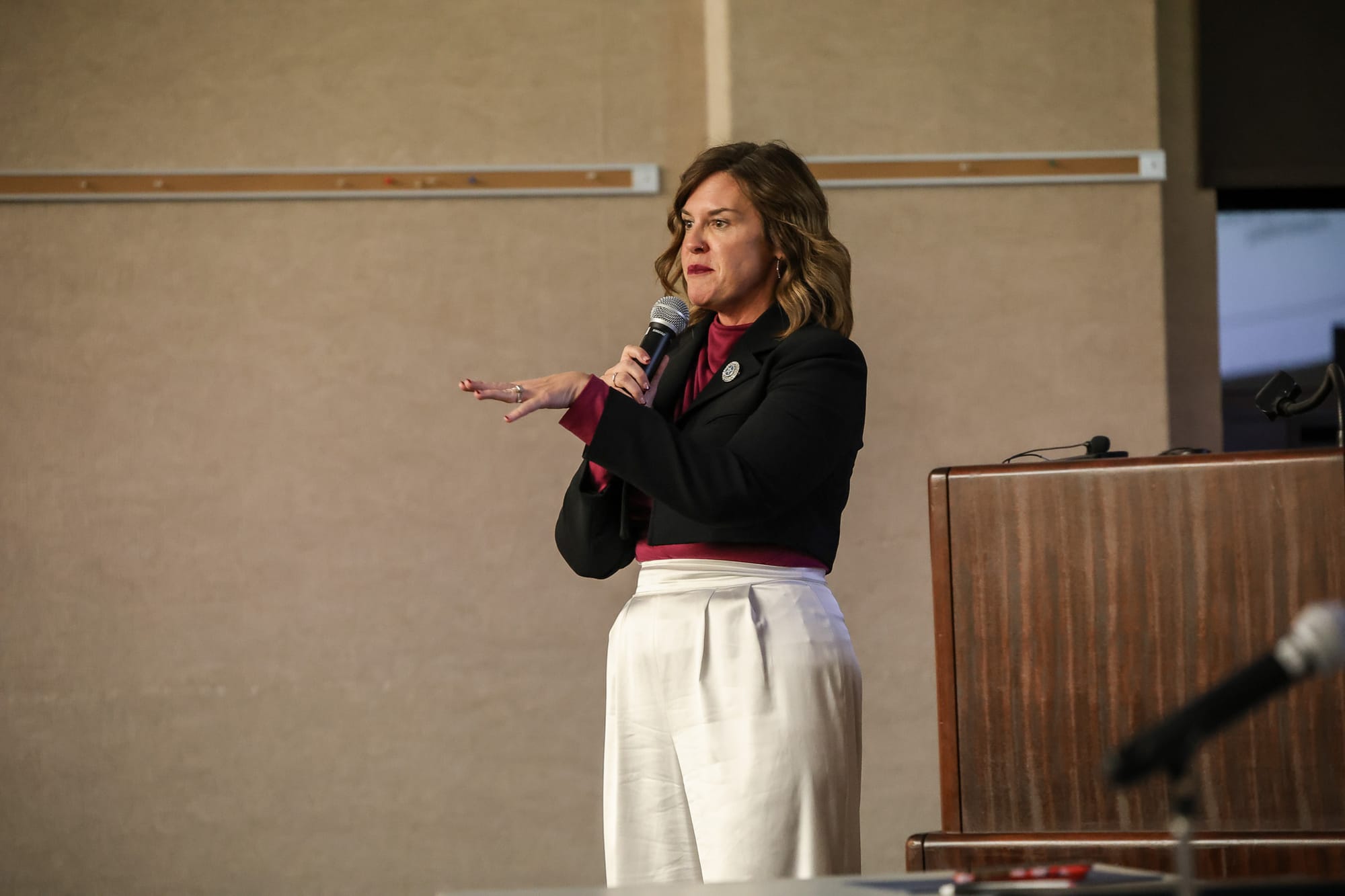 Leslie Clingenpool addresses audience while holding microphone, standing near podium at community panel discussion at Stillwater Public Library.
