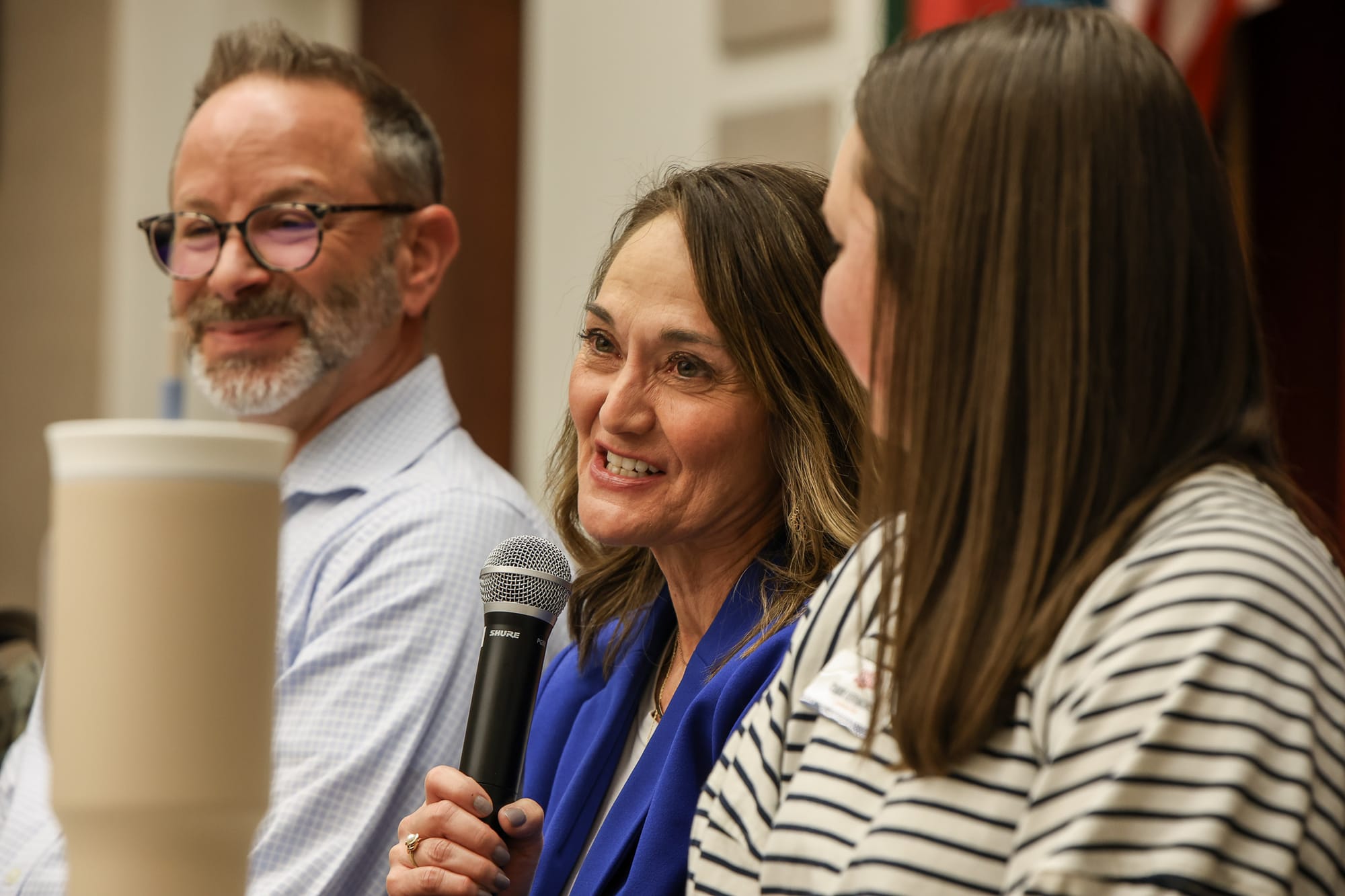 Mary Melton smiles while holding a microphone during a panel discussion, seated between fellow panelists at Stillwater Public Library.
