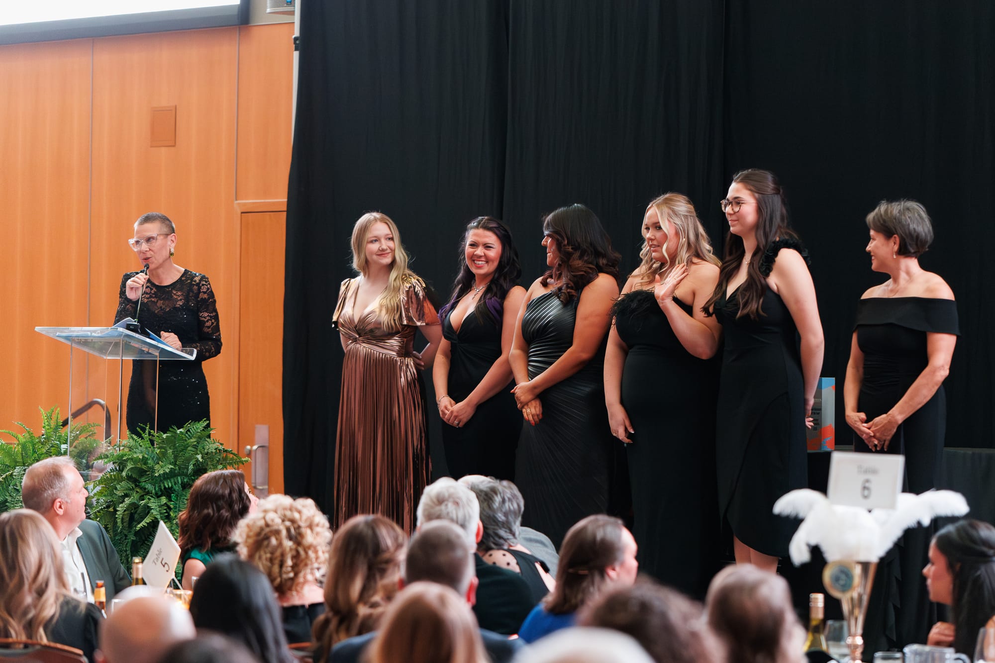 Alane Zannotti speaks at a podium as six Chamber staff members stand on stage behind her during the Stillwater Chamber of Commerce Awards Gala. 