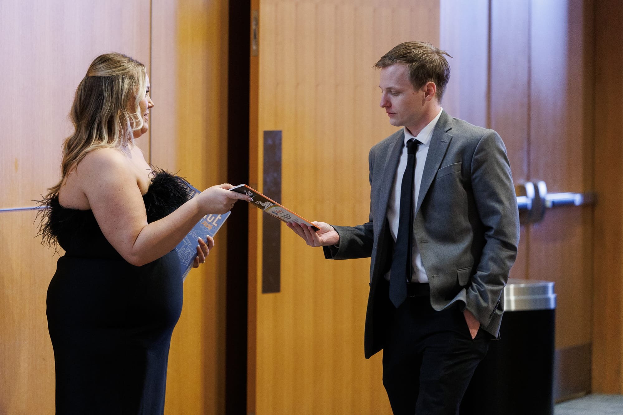 Grace Impson hands a copy of the Chamber's Commerce Magazine to a male guest in a gray suit at the Stillwater Chamber of Commerce Awards Gala.
