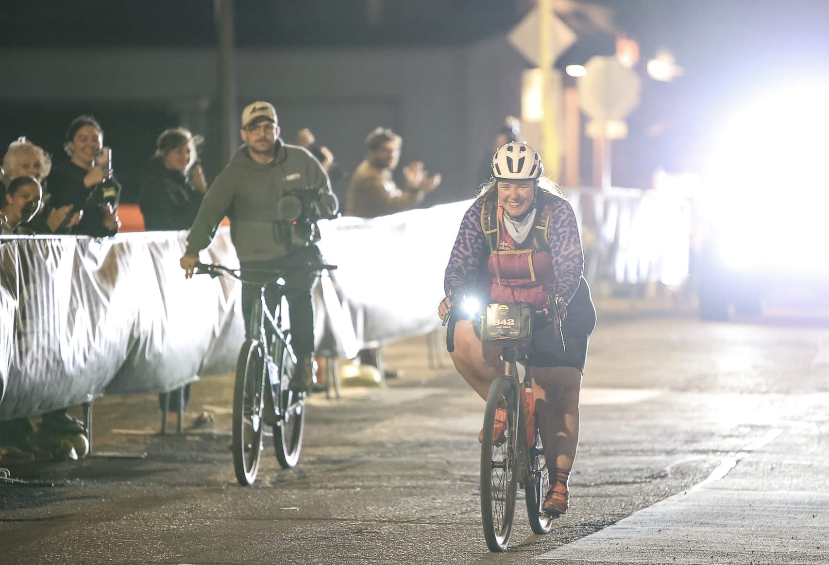 Owenreay rides down the Mid South finish line chute at night on March 14, 2026, smiling, with Jeep headlights glowing behind her in Stillwater.