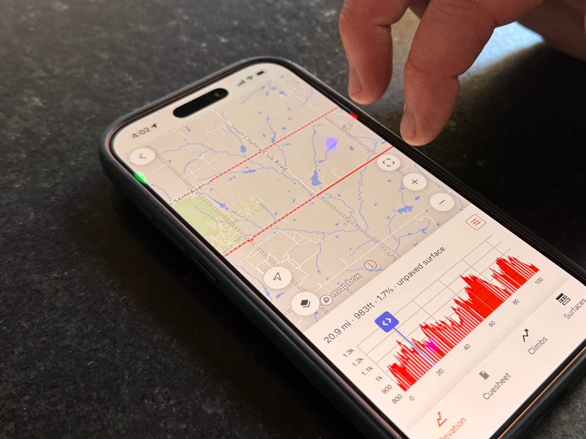 Bobby Wintle points at an iPhone showing the 2026 Mid South 100-mile route and elevation profile on RideWithGPS, with the steepest climbs concentrated in the final miles.