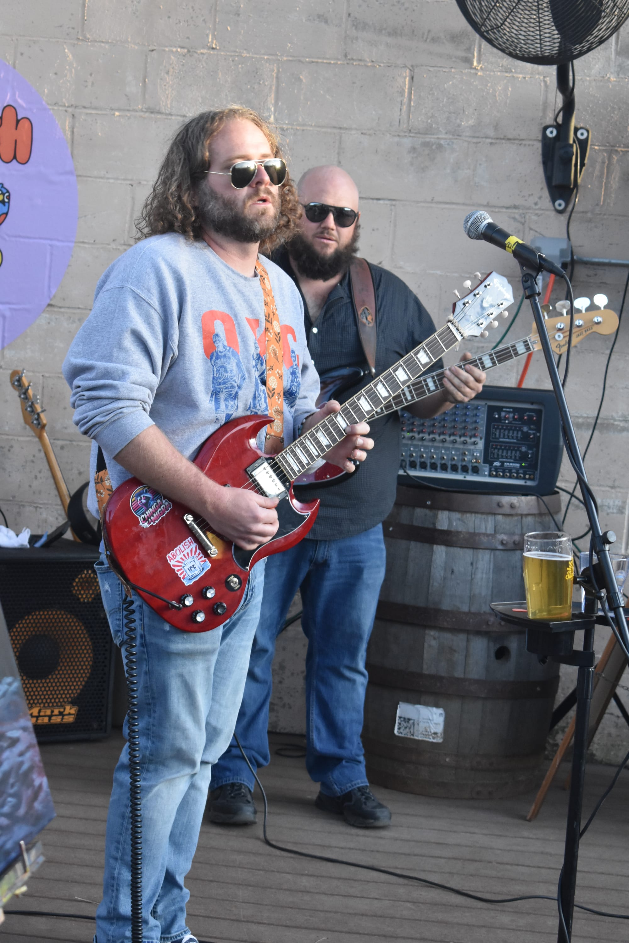Kurtis Brock Hair plays a red electric guitar at the Stonecloud Brewing patio stage, with bassist Felix Miller visible behind him. 