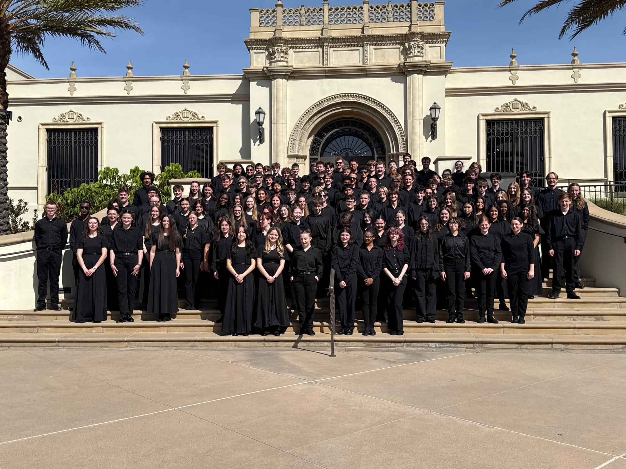 More than 100 Stillwater High School band students in black attire pose on the steps of a Spanish Renaissance building at the University of San Diego.