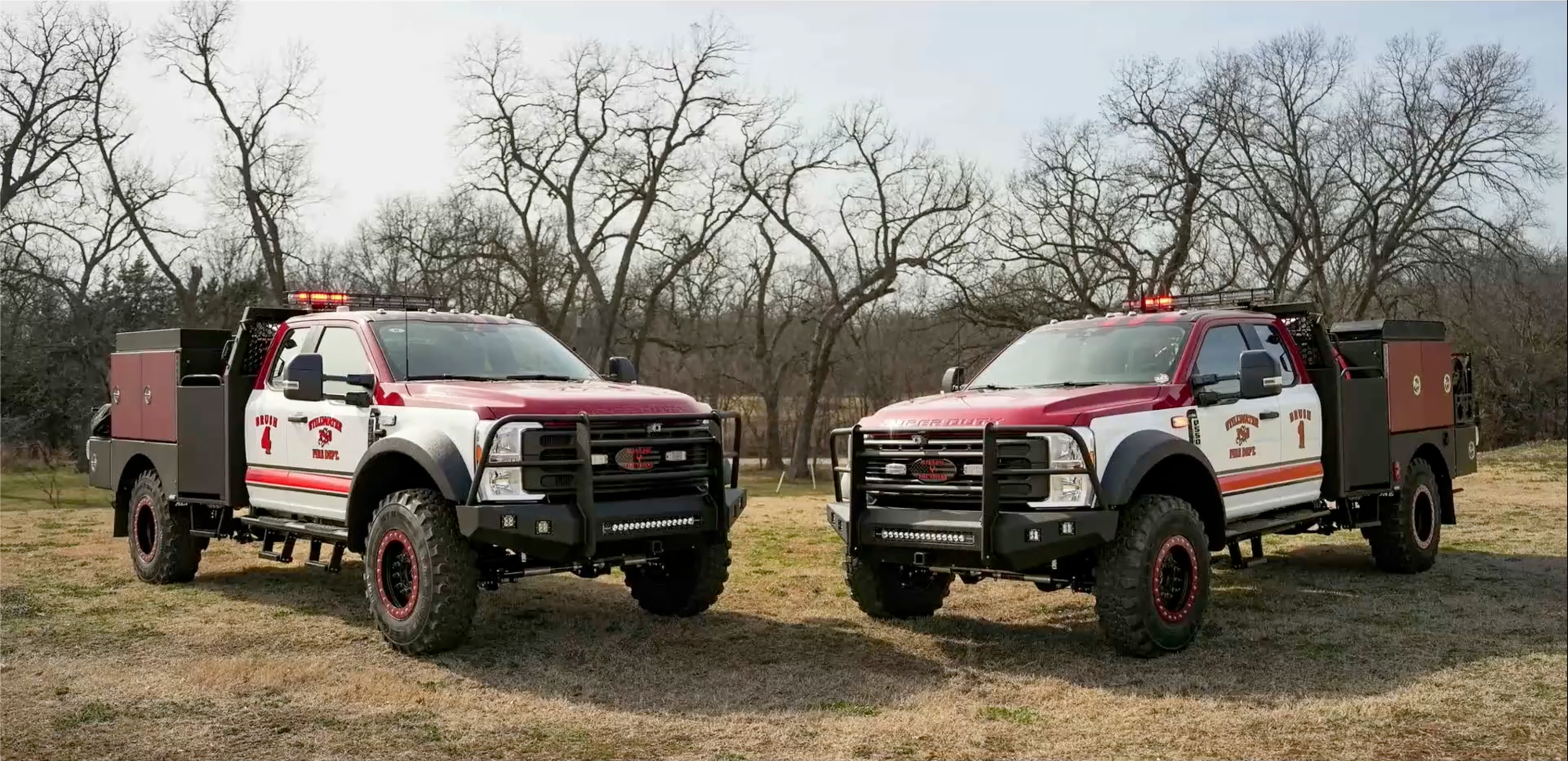 Two red and white Stillwater Fire Department brush trucks, numbered Brush 4 and Brush 1, parked facing each other outdoors with bare trees in the background.