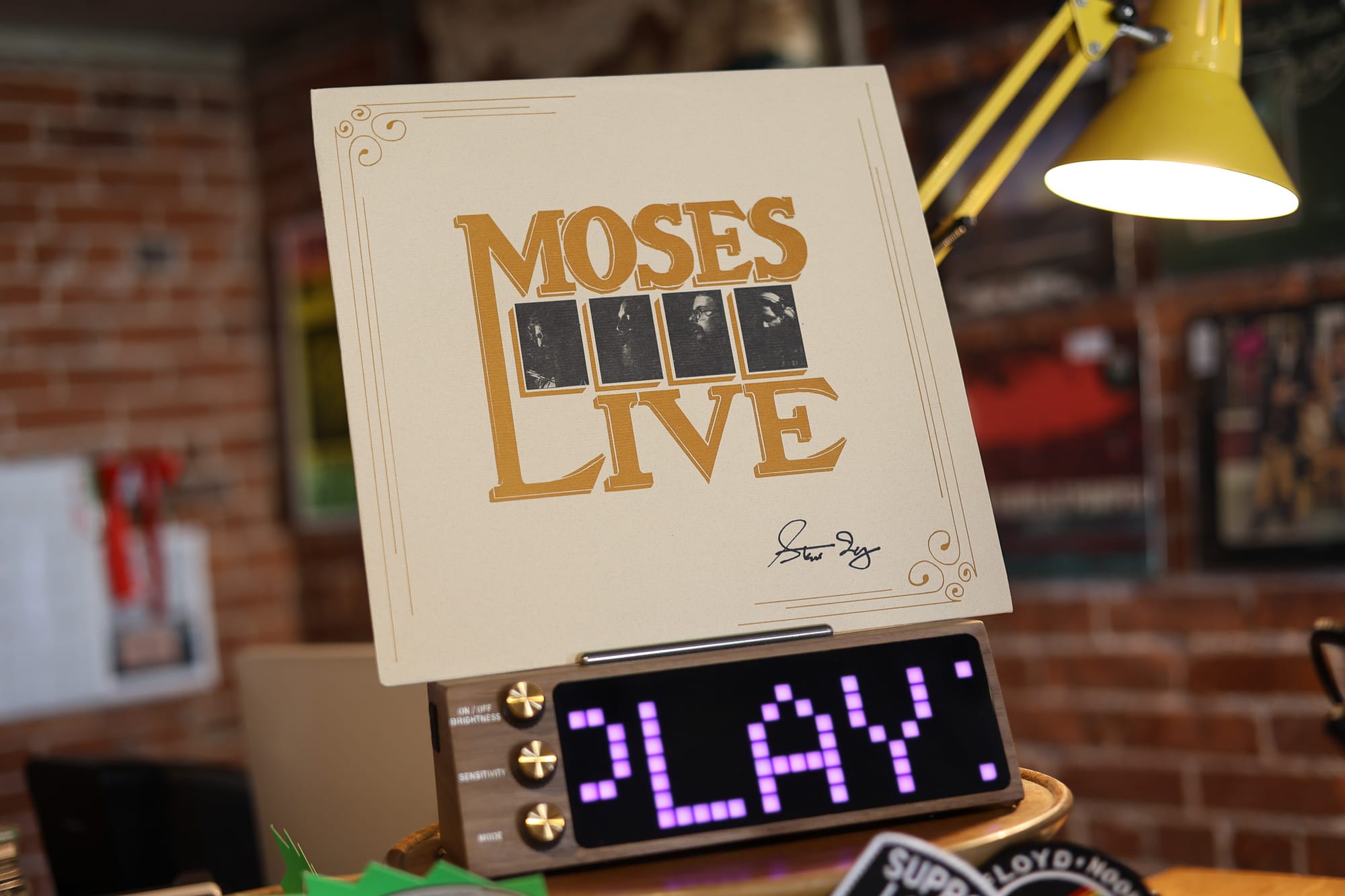 Signed Moses Live album cover displayed at Velvet Fudge, showing black-and-white photos of four band members with Steve Irby third from left, digital display below scrolling NOW PLAYING.